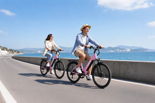 Man and woman riding pink Eskute step-through e-bikes along seaside highway, blue sea and mountain backdrop, relaxed leisure cycling trip